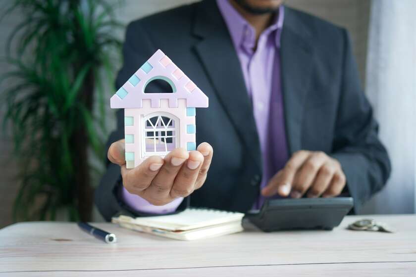 Un homme qui tient dans sa main une maison et qui tape avec l'autre sur une calculatrice