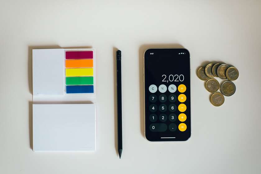 Un smartphone ouvert sur l'application calculatrice, un bloc note et un stylo