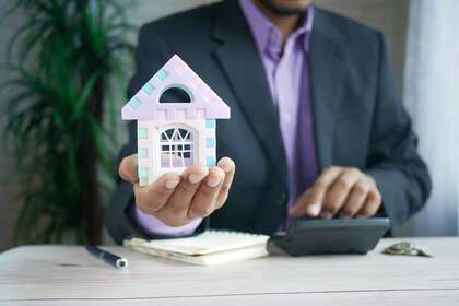 Un homme qui tient dans sa main une maison et qui tape avec l'autre sur une calculatrice